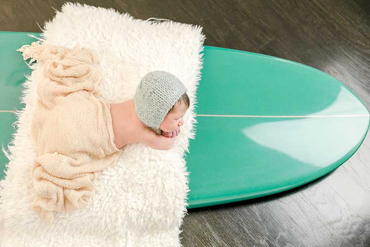 A newborn fast asleep on a surfboard.