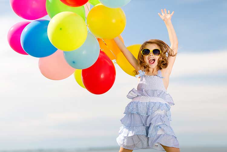 A girl dances while holding on to a bunch of balloons at a photoshoot.