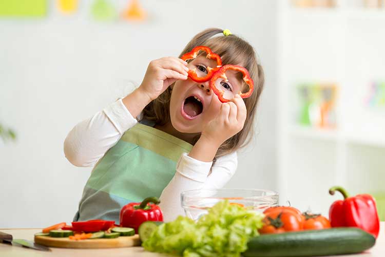 A young girl holds up pepper rings like spectacle frames.