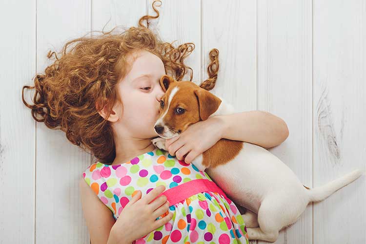 A young girl kisses her baby puppy.