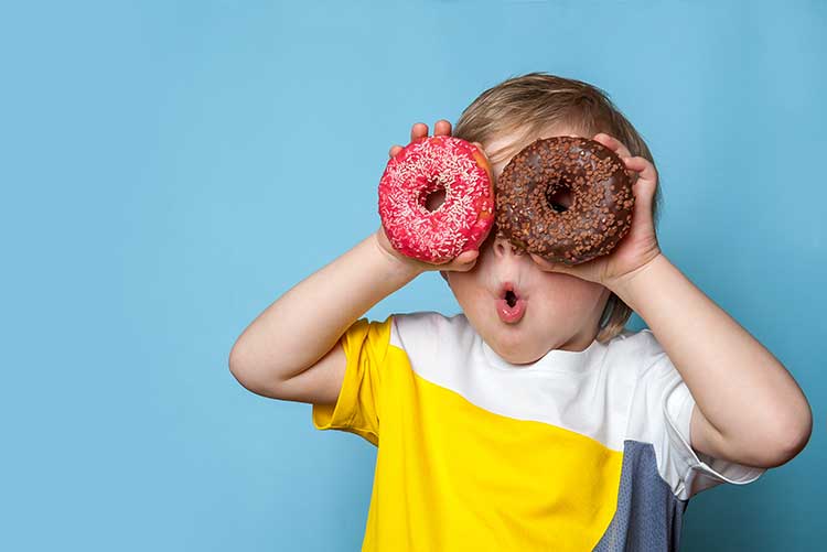 A baby boy pretends two big donuts to be eyes.